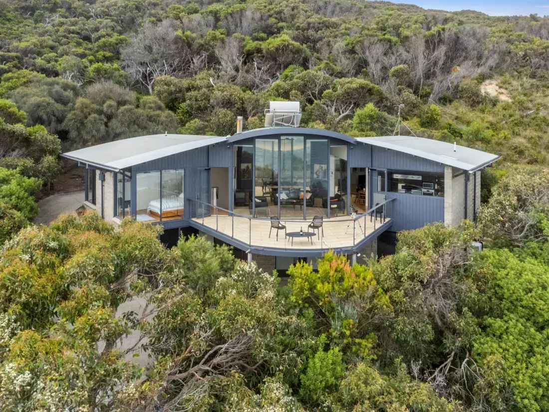 A modern house sits among dense green trees and shrubs.