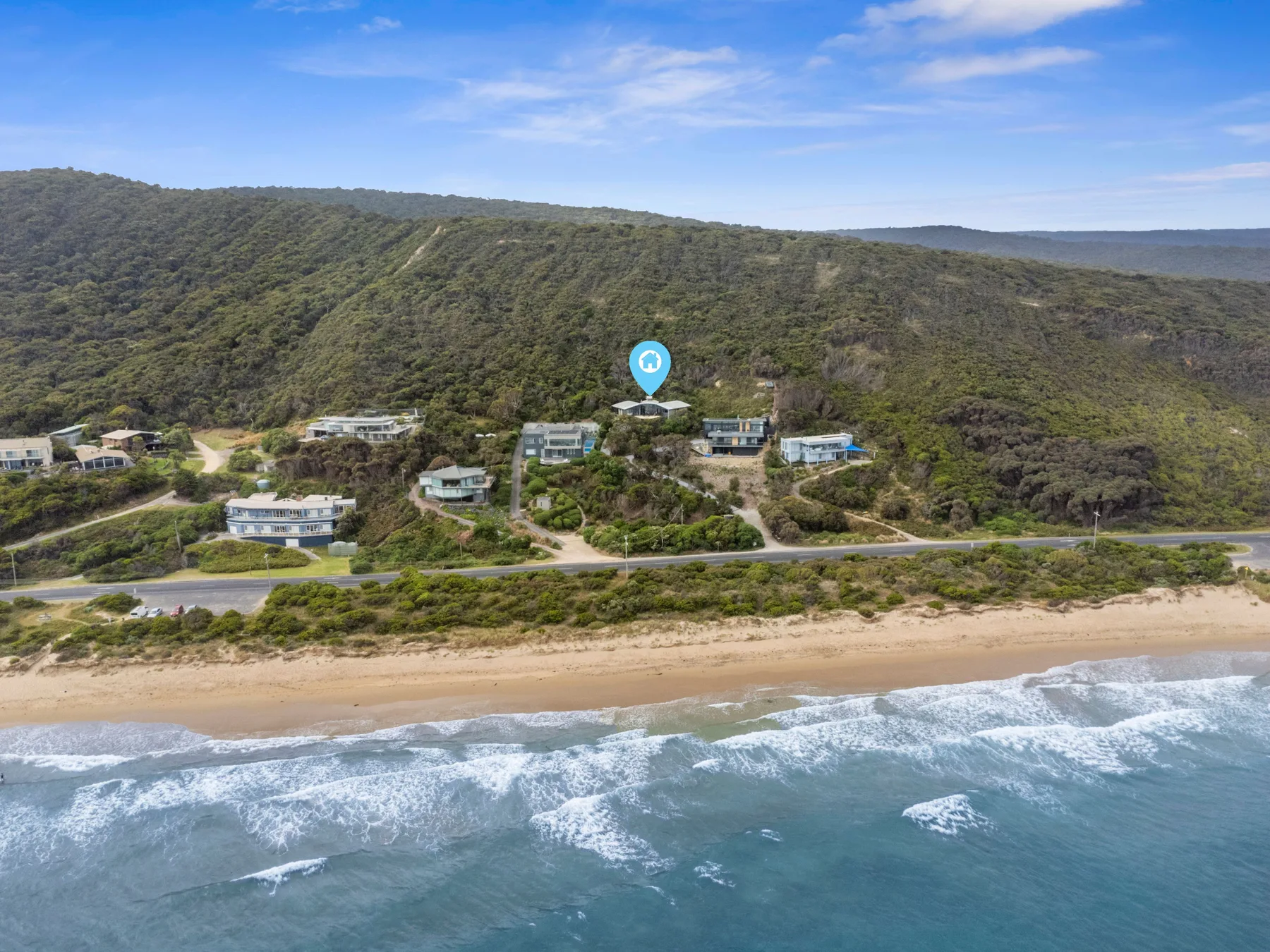 Aerial view of a coastal settlement between a wooded hillside and a sandy beach.