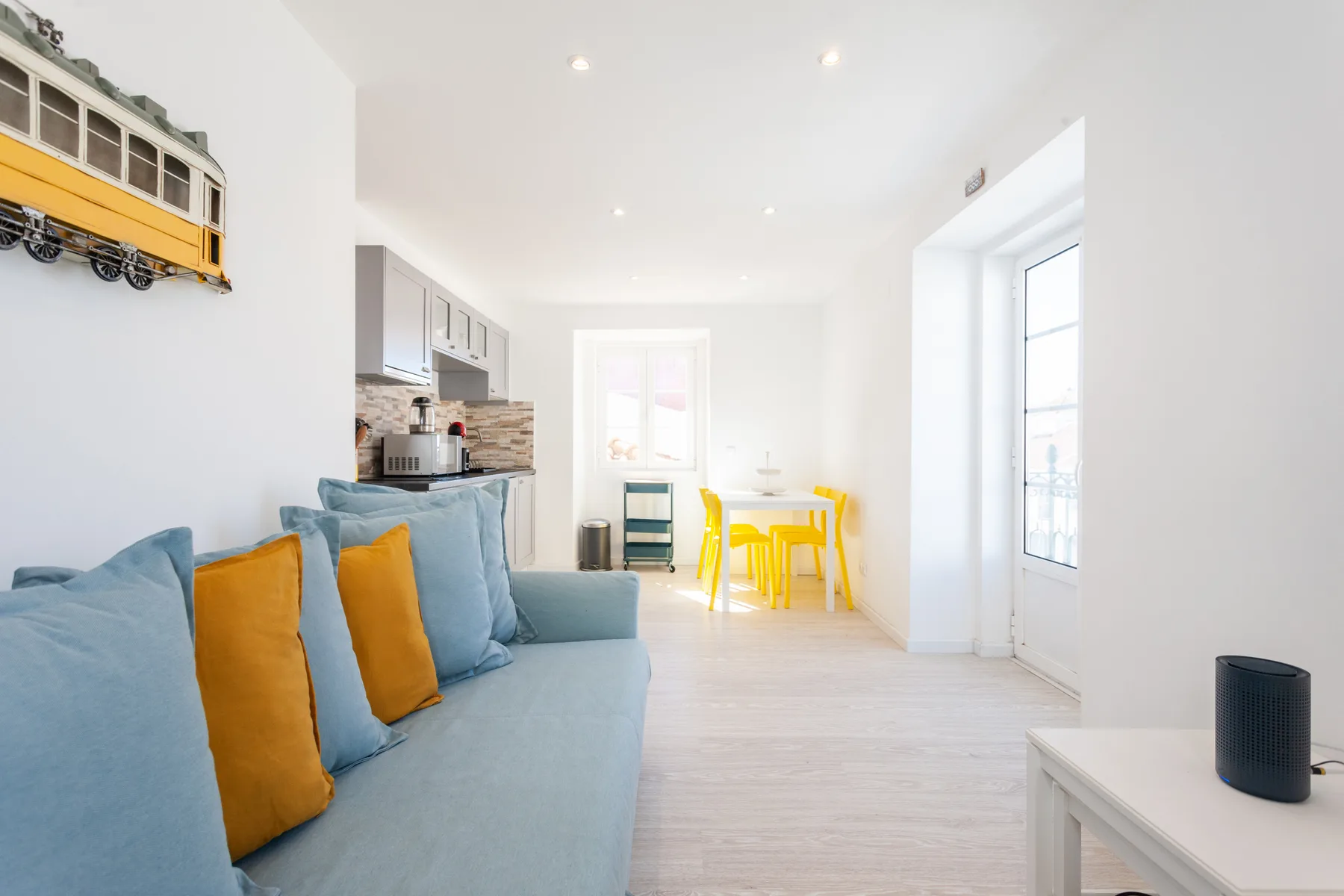 Una luminosa sala de estar y comedor con asientos azules y una mesa amarilla.