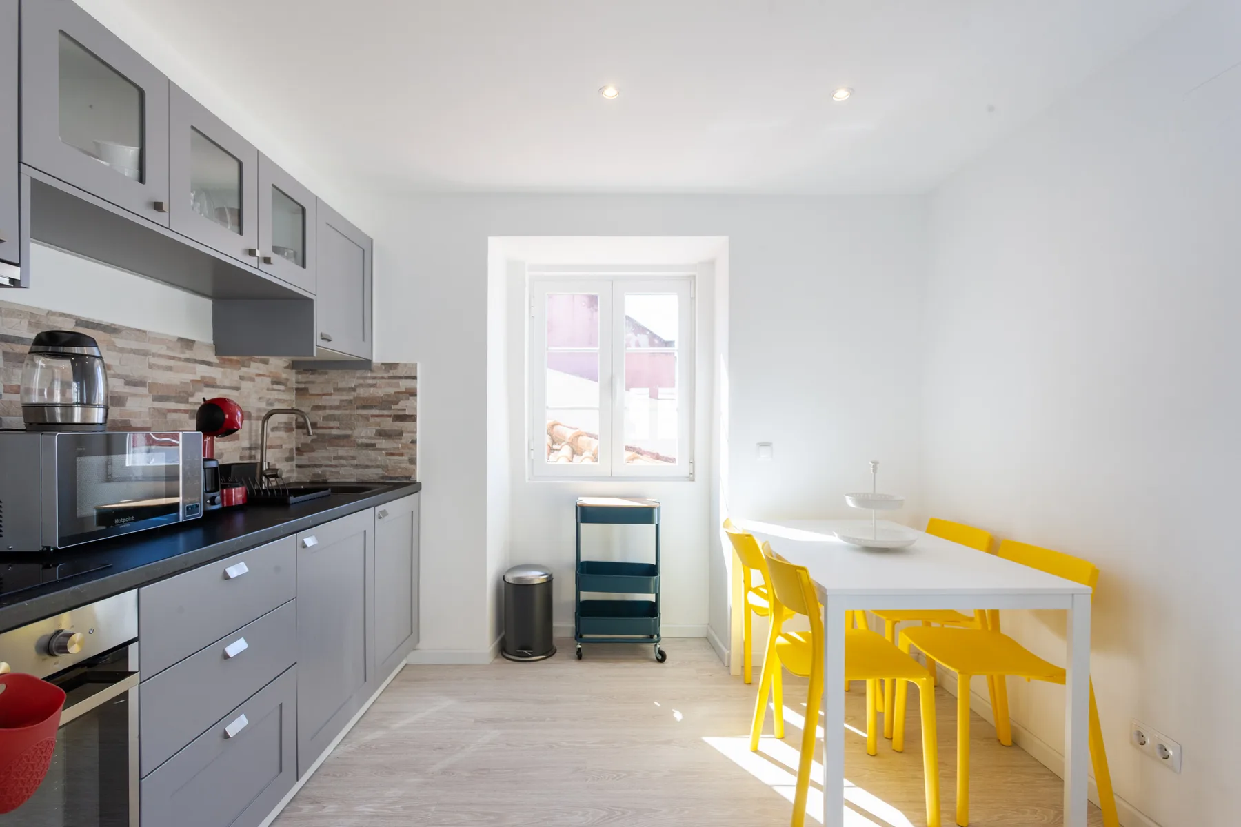 Una cocina luminosa con zona de comedor, armarios grises y asientos amarillos.