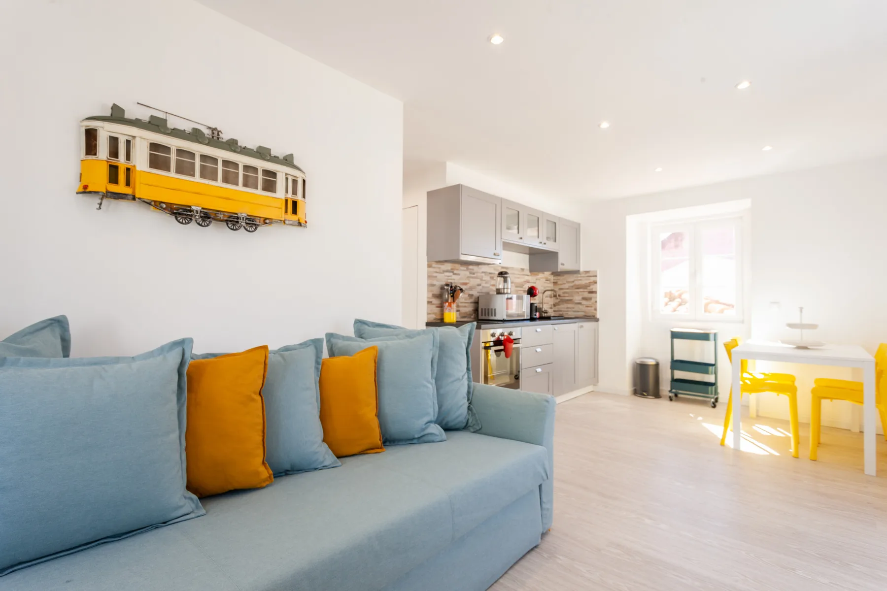 Una sala luminosa con asientos azules junto a una cocina compacta y una mesa de comedor.