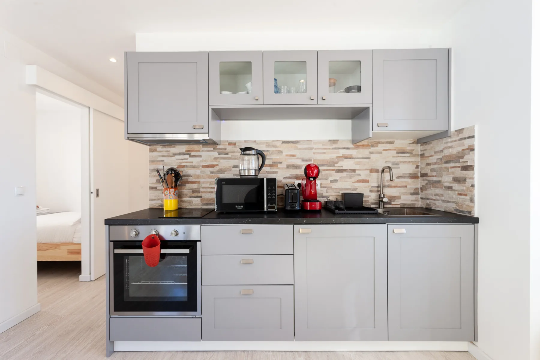 Una cocina moderna con gabinetes grises, electrodomésticos sobre la encimera y horno integrado.
