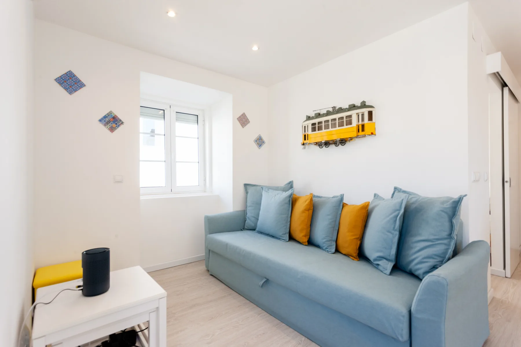 Una sala de estar con asientos azules, cojines de colores y una ventana.