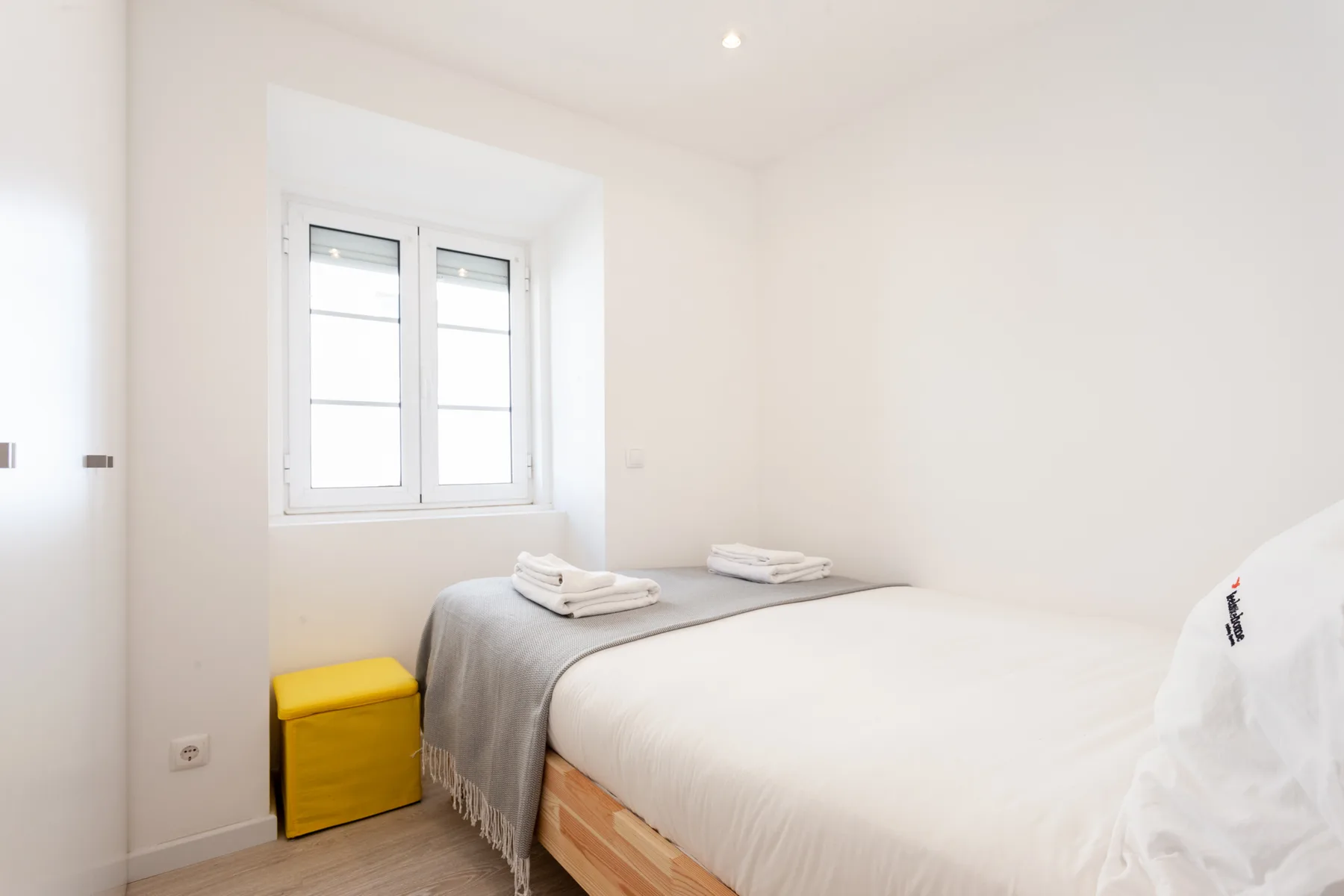 Un dormitorio luminoso con una cama, toallas dobladas y una ventana.