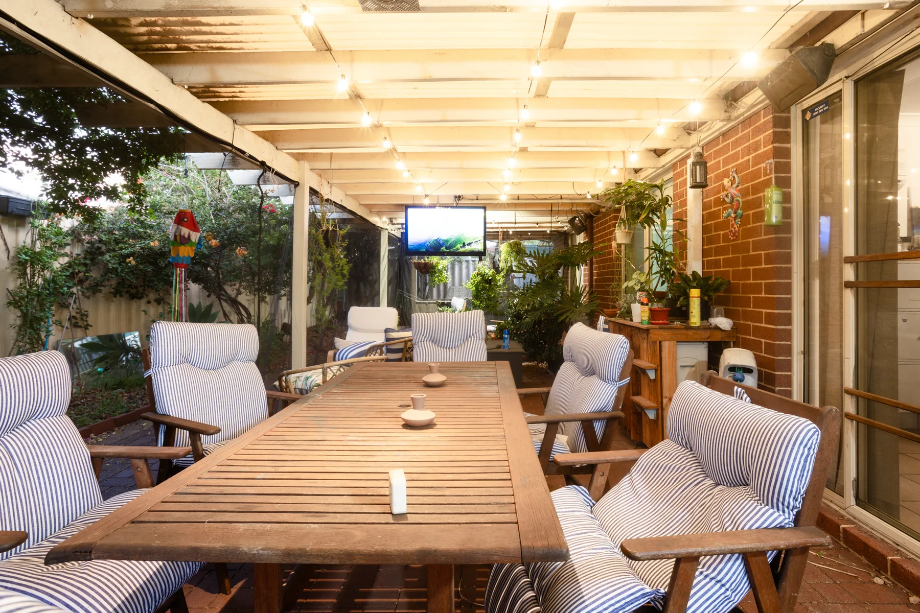 A covered patio with a long wooden table and cushioned seating.