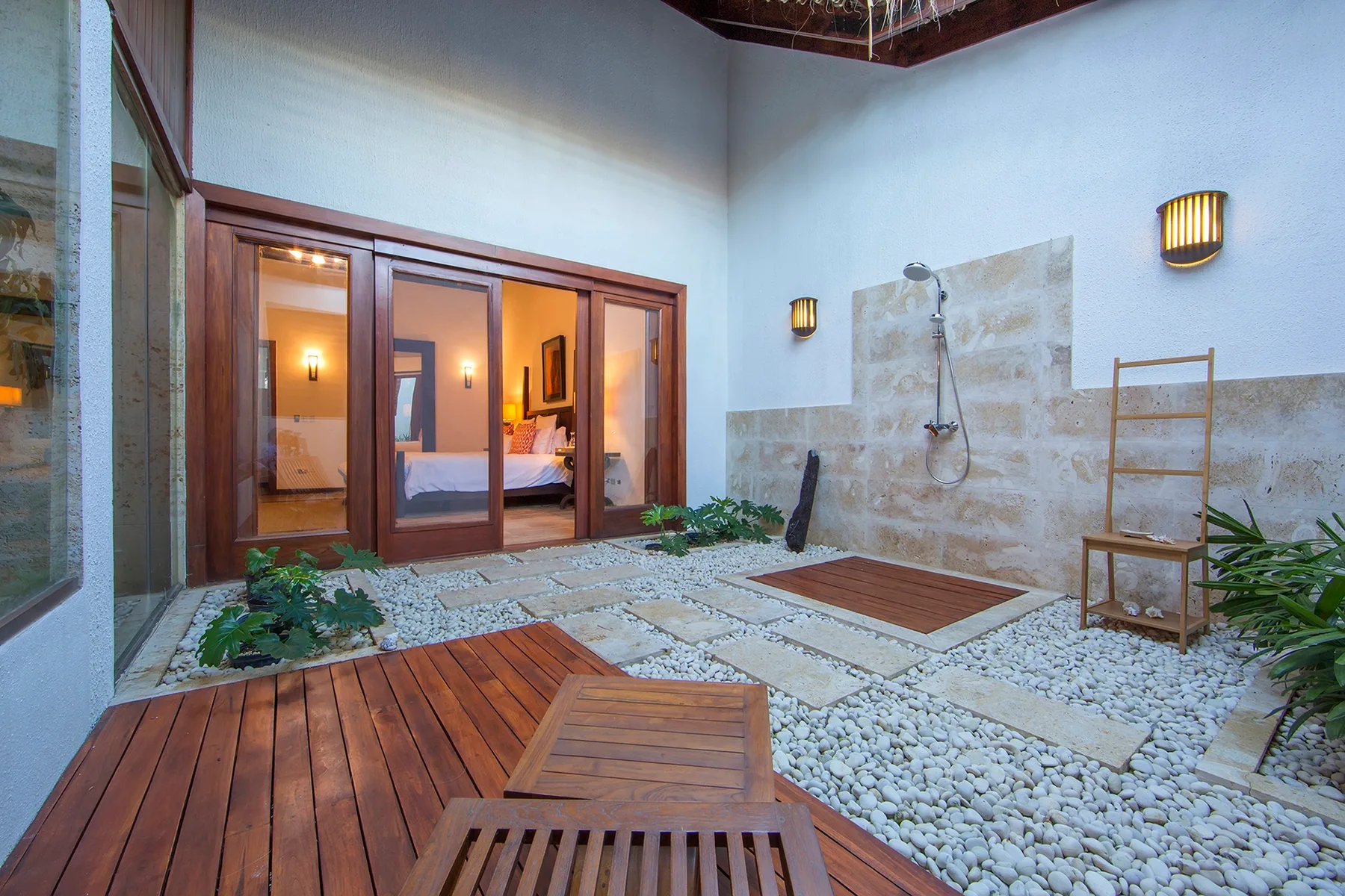 Una zona de ducha exterior con una terraza de madera y suelo de guijarros.