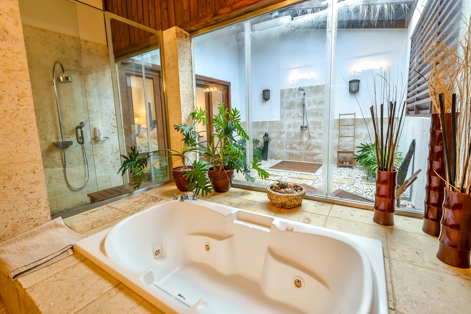Un baño con una bañera grande, una ducha de vidrio y plantas en macetas.
