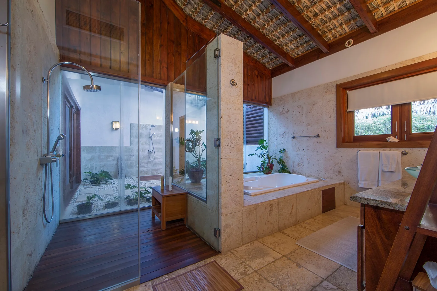 Un baño con una zona de ducha de vidrio y una bañera bajo una ventana.