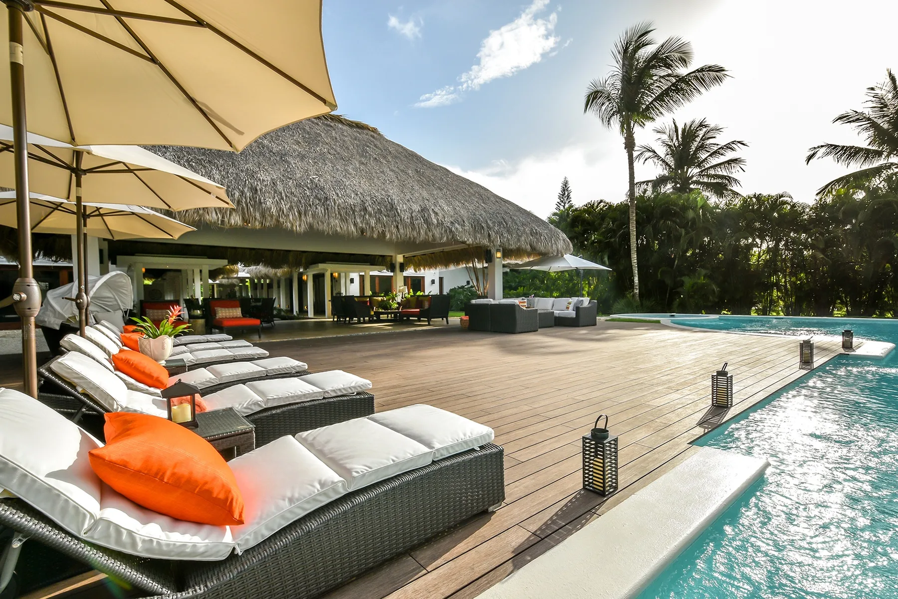 Un patio junto a la piscina con asientos acolchados junto a un edificio con techo de paja.