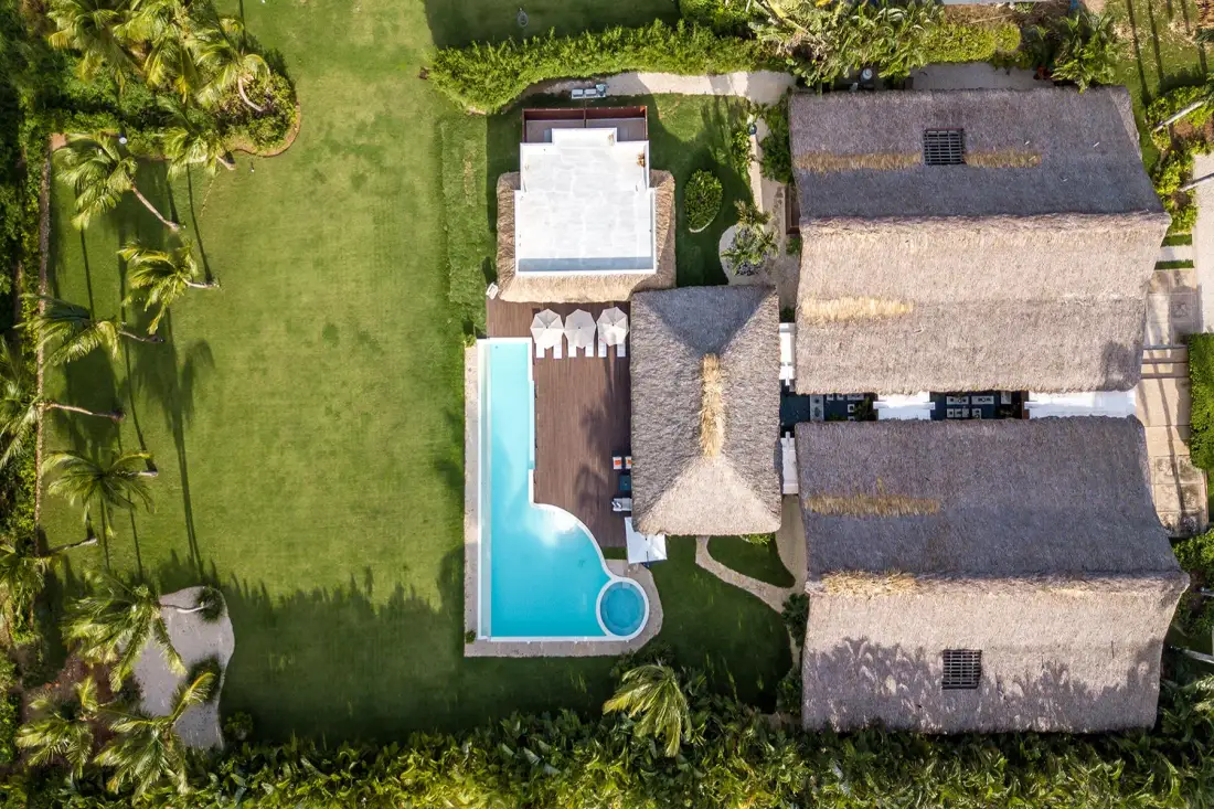 Vista aérea de una propiedad tropical con una piscina turquesa y edificios con techo de paja.