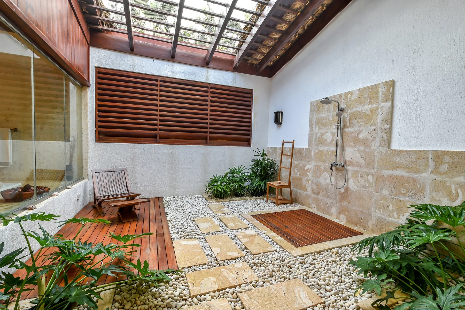 Una zona de ducha al aire libre con una pared de piedra, tarima de madera y plantas.