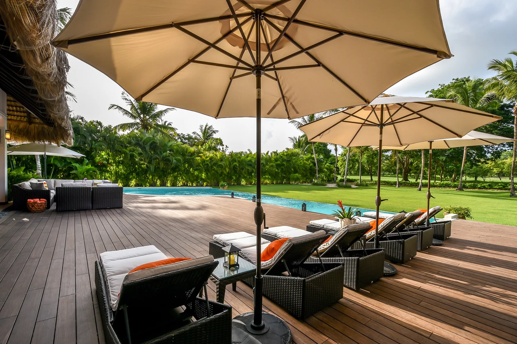 Una terraza junto a la piscina con asientos reclinables y sombrillas grandes.