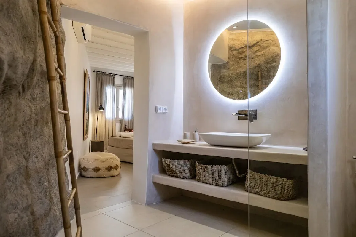 Un mueble de baño con lavabo de sobreponer y espejo redondo iluminado.