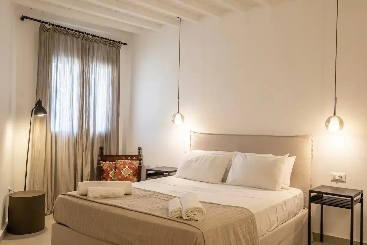 Un dormitorio con una cama bien hecha y cortinas translúcidas.