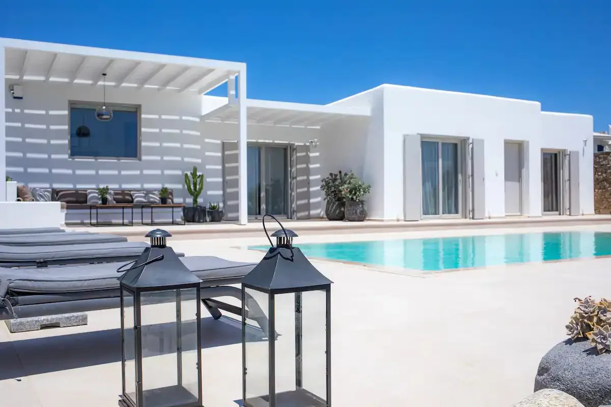 Una villa blanca moderna con piscina y patio sombreado.