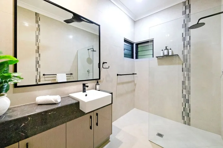 Un baño luminoso con lavabo, espejo grande y ducha a ras de suelo.
