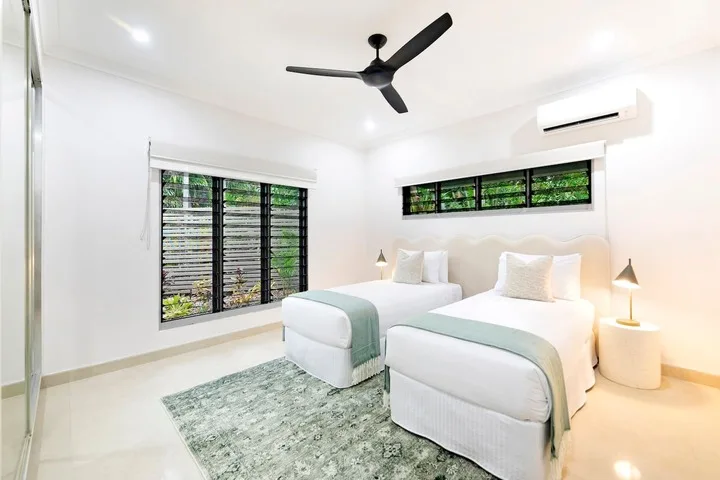 Un dormitorio luminoso con dos camas, ropa de cama clara y ventanas amplias.