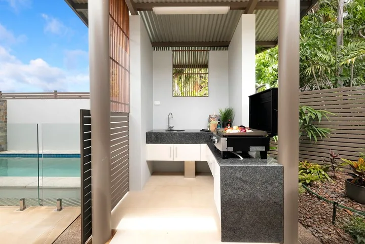 Una cocina al aire libre con encimera y fregadero da a una piscina.