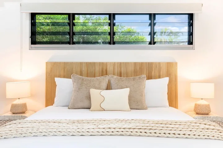 Un dormitorio con una cama bien arreglada bajo una ventana amplia.