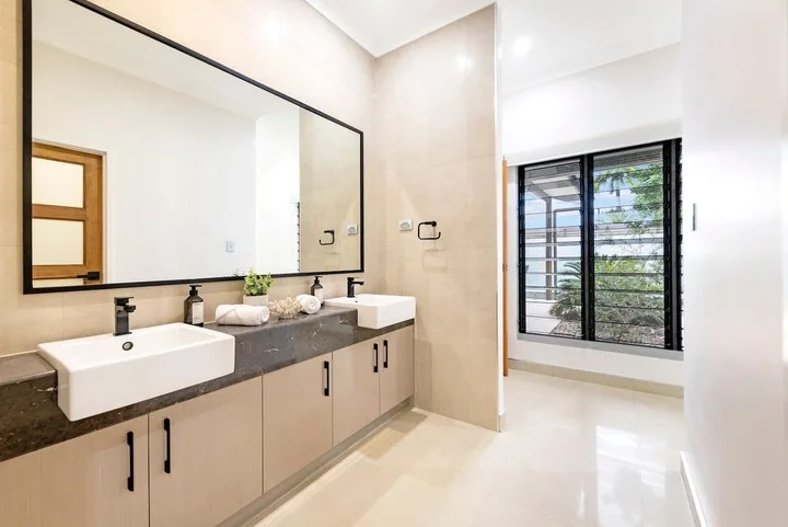 Un baño luminoso con un largo tocador, un espejo amplio y una ventana.