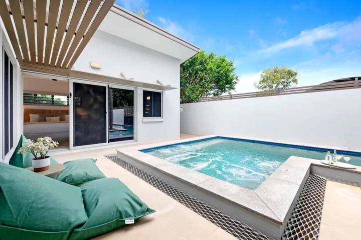 Una pequeña piscina exterior junto a un patio con asientos acolchados.