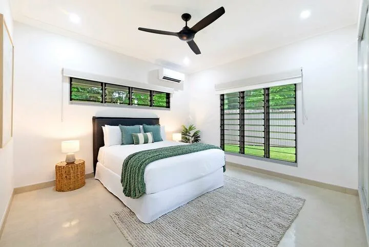 Un dormitorio luminoso con una cama bien arreglada y grandes ventanas.