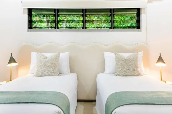 Un dormitorio con dos camas y una ventana estrecha encima.