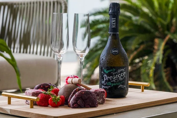 Una presentación de bebidas con una botella, dos copas y fruta en una bandeja.