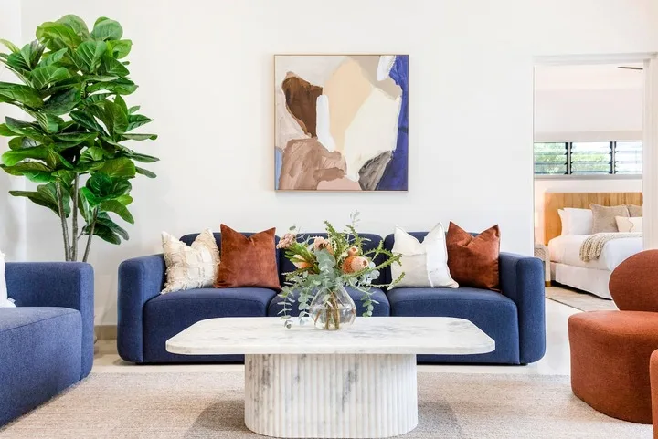 Una sala de estar con un sofá azul, una mesa de centro y una planta frondosa.