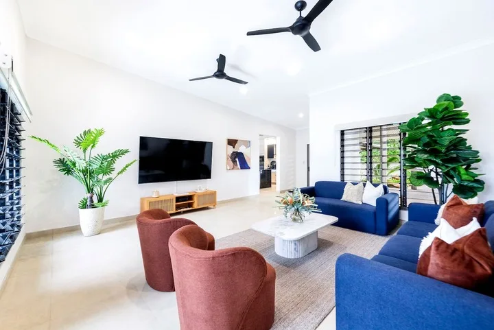 Una sala luminosa con asientos azules, un televisor y plantas.