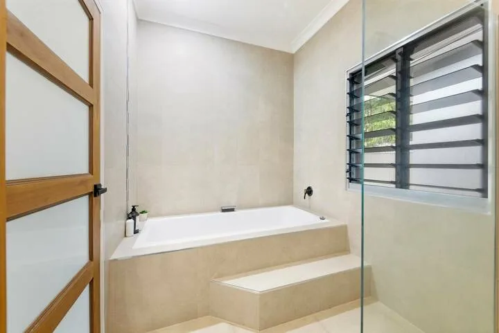 Un baño con una bañera empotrada y una ventana con lamas horizontales.