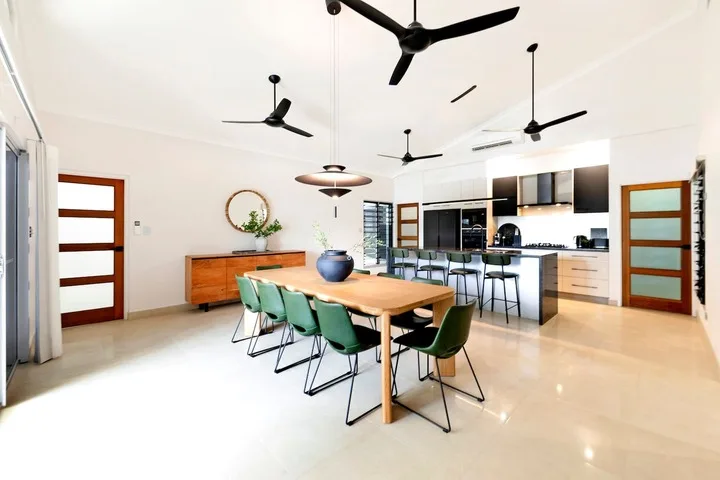 Comedor con una mesa larga y asientos verdes junto a una cocina abierta.