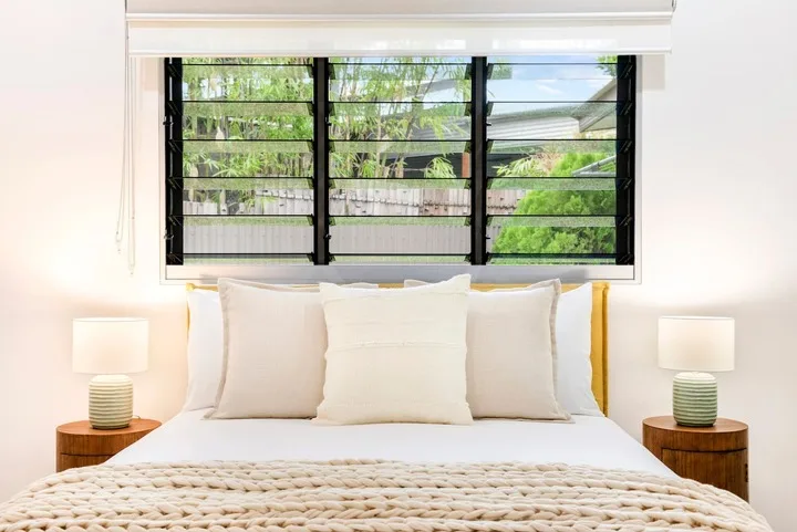 Un dormitorio con una cama bien arreglada bajo una ventana amplia.