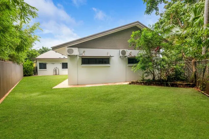 Una casa blanca se encuentra junto a un amplio césped verde, con árboles alrededor del patio.