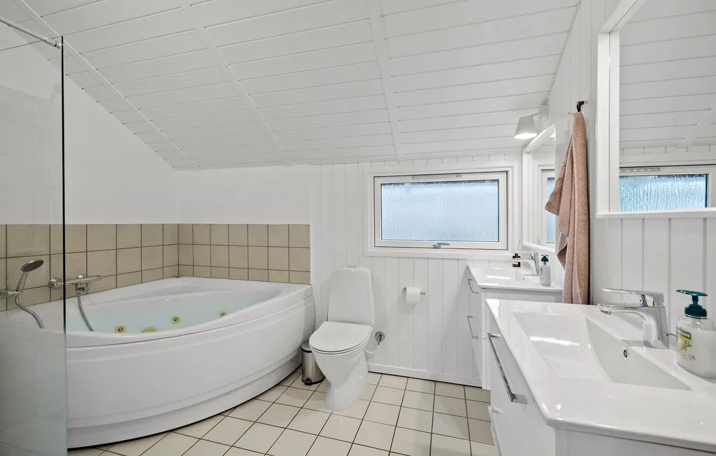A bright bathroom with a corner bathtub, toilet, and sinks.