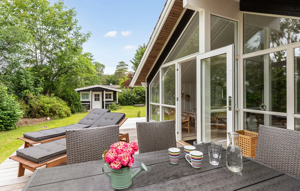 An outdoor patio dining area overlooks a green lawn and a glass-walled house.