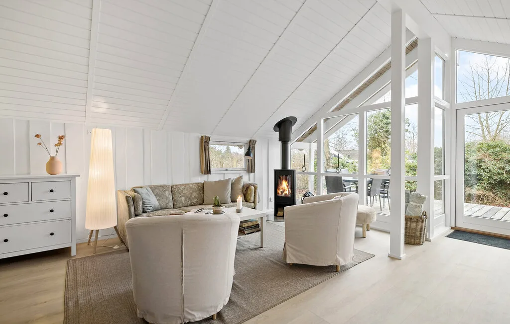 A bright living room with seating and a wood-burning stove beside large windows.