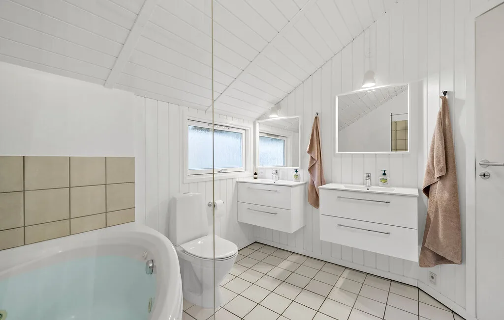 A bright bathroom with a bathtub, toilet, and wall-mounted sink cabinets.