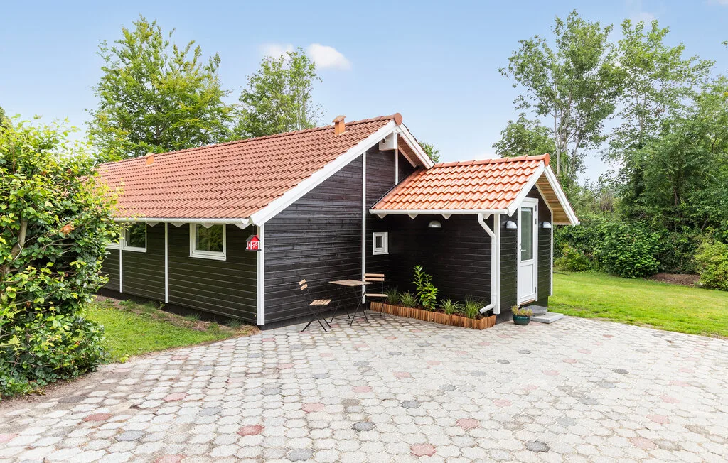 A dark wood cabin with red tiled roofs stands beside a paved courtyard and green lawn.