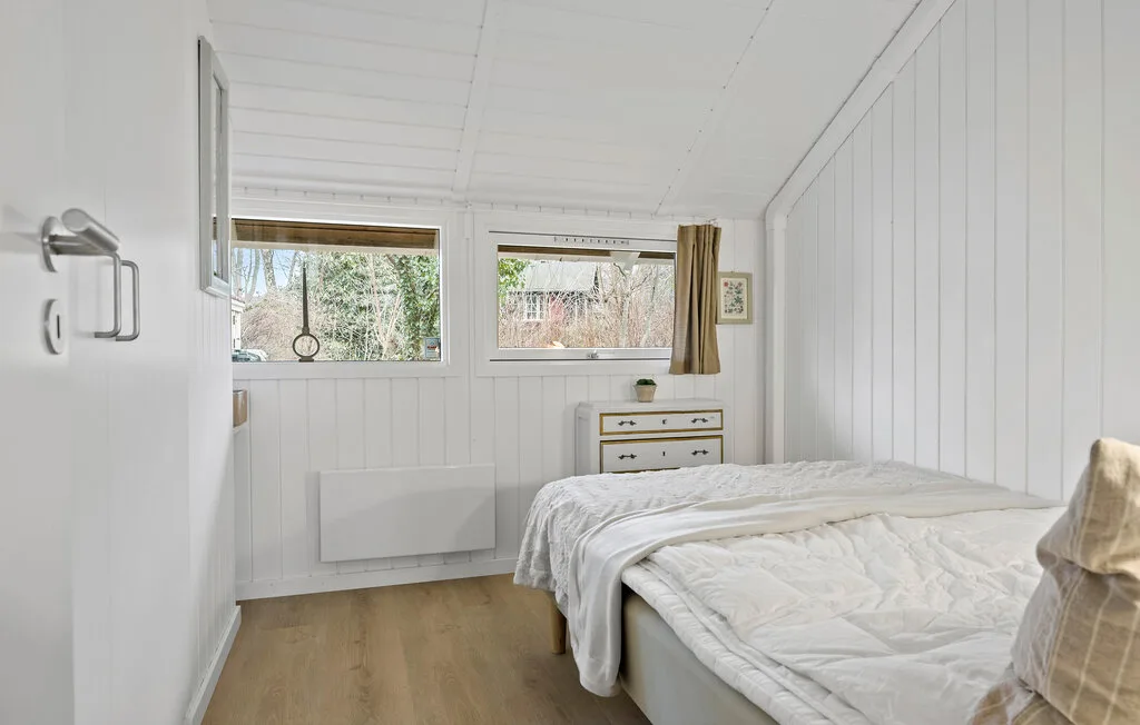 A bright bedroom with a bed beneath two windows.