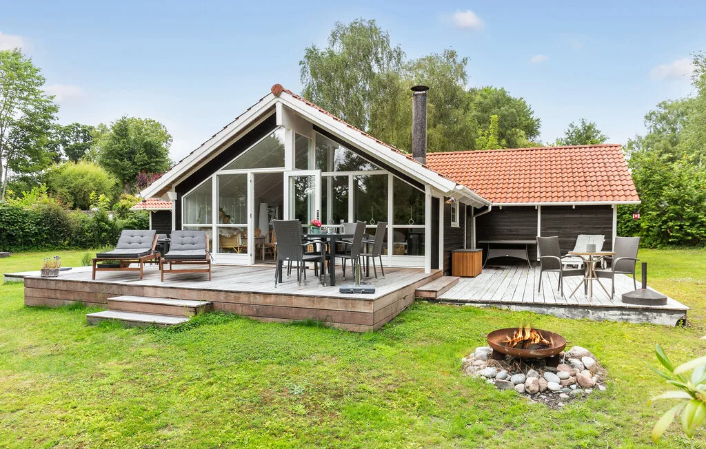 A glass-fronted house opens onto a deck with outdoor seating and a lawn.