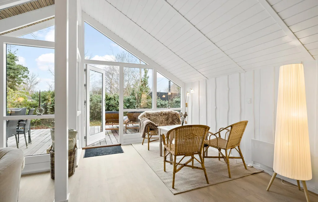 A bright sunroom with wicker seating beside large windows overlooking a garden.