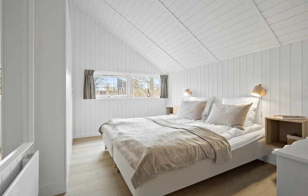 A bright bedroom with a bed beneath a sloped white ceiling.