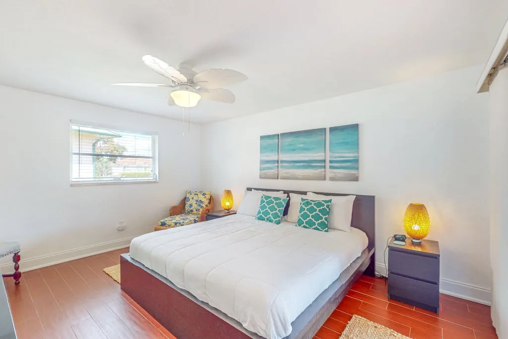 A bright bedroom with a neatly made bed and beach artwork above it.
