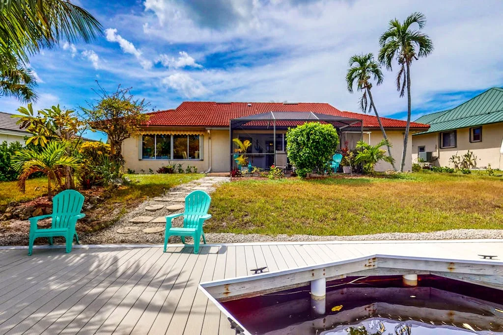 A house and yard with a wooden deck and swimming pool in the foreground.