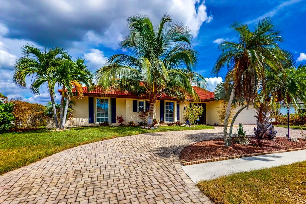 A single-story house with a paved driveway and palm trees.