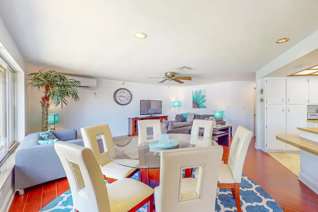 A bright dining and living area with a glass table and white seating.