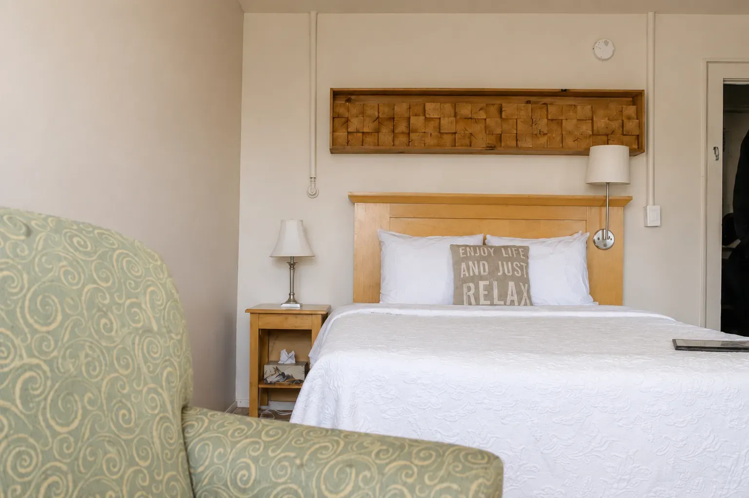 Hotel room with two beds, green chairs, exposed wooden beam, and window with curtains