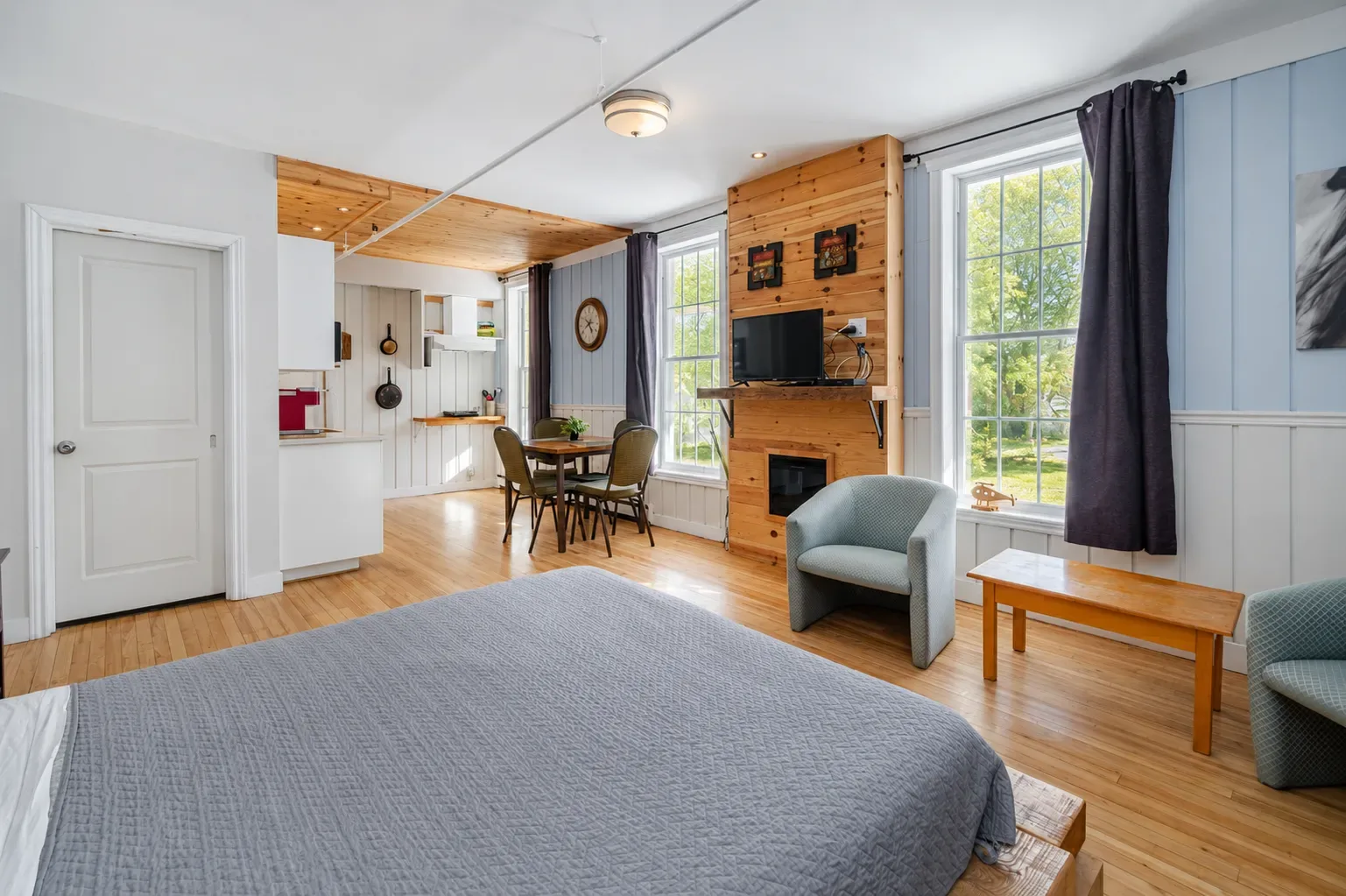 Bright bedroom with a bed, red floral art, large windows, and wooden floors
