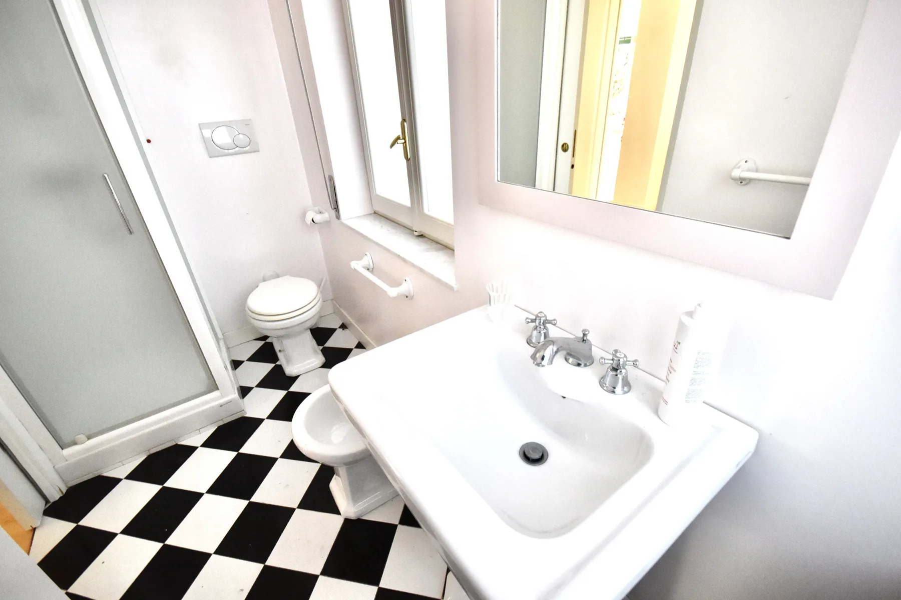 A bright bathroom with a sink, toilet, and black-and-white checkered floor.